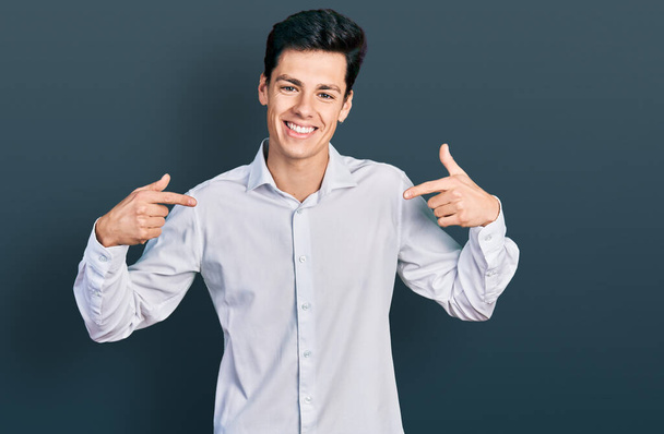 Joven hombre de negocios hispano vistiendo ropa de negocios que se ve confiado con sonrisa en la cara, señalándose con los dedos orgullosos y felices.  - Foto, Imagen