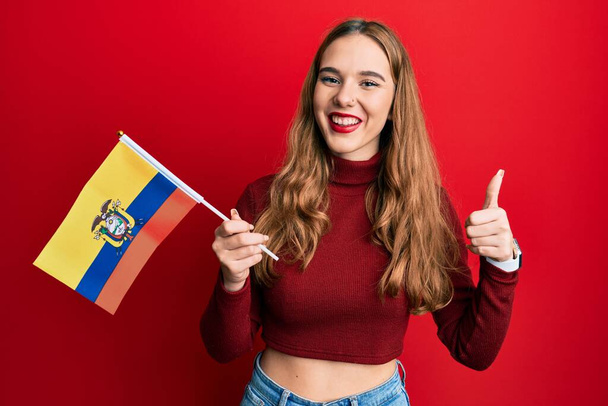Mladá blondýnka drží ecuador vlajku s úsměvem šťastný a pozitivní, palec nahoru dělá vynikající a schvalovací znamení  - Fotografie, Obrázek