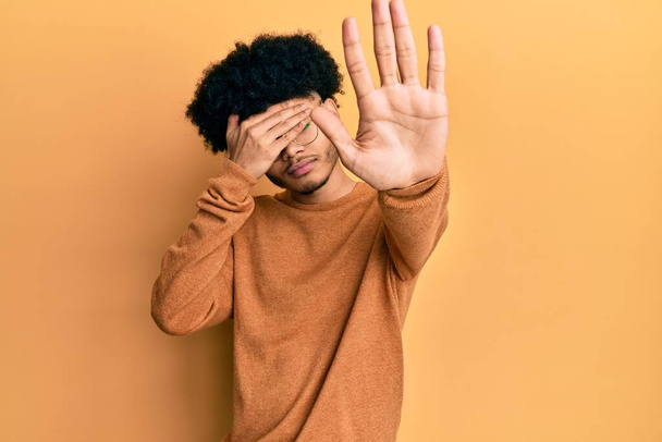 Giovane uomo afro americano con i capelli afro indossa casual maglione invernale che copre gli occhi con le mani e facendo fermare il gesto con espressione triste e paura. concetto imbarazzato e negativo.  - Foto, immagini