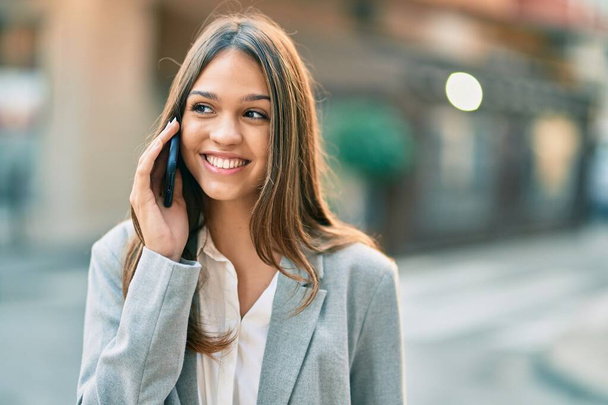 Молодая латинская бизнесвумен улыбается счастливо разговаривая на смартфоне в городе. - Фото, изображение