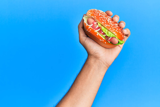 Kéz a spanyol férfi tartja hot dog felett elszigetelt kék háttér. - Fotó, kép