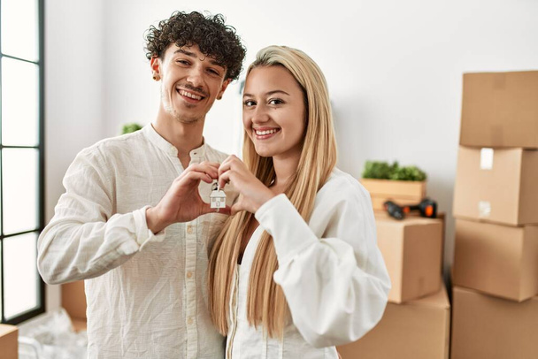 Joven hermosa pareja haciendo símbolo del corazón con los dedos y sosteniendo la llave de un nuevo hogar. - Foto, Imagen