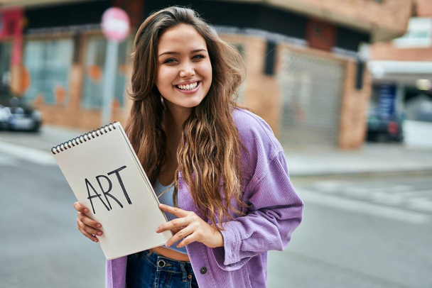 Молодая испаноязычная студентка улыбается счастливо держа блокнот в городе. - Фото, изображение