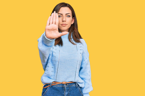 Young brunette woman wearing casual winter sweater doing stop sing with palm of the hand. warning expression with negative and serious gesture on the face.  - Photo, Image