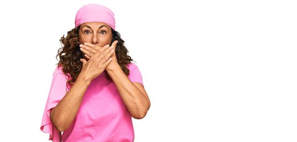 Hispánka středního věku nosící rakovinu prsu podpírá růžový šátek, který zakrývá ústa rukama, aby nedošlo k omylu. tajný koncept.  - Fotografie, Obrázek