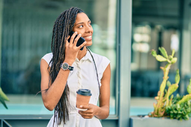 Joven mujer afroamericana hablando en el teléfono inteligente y bebiendo llevar café en la ciudad. - Foto, Imagen