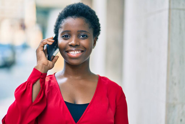 Молода афроамериканська жінка, яка посміхається, радісно розмовляє на смартфоні міста.. - Фото, зображення