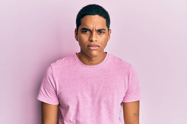 Young handsome hispanic man wearing casual pink t shirt skeptic and nervous, frowning upset because of problem. negative person.  - Foto, Imagen