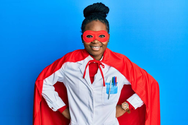 Jeune femme afro-américaine portant l'uniforme de médecin et costume de super héros souriant avec un sourire heureux et cool sur le visage. montrant les dents.  - Photo, image
