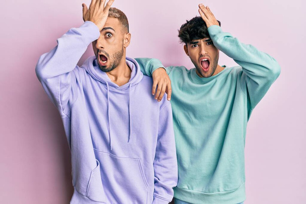 Homosexual gay couple standing together wearing casual clothes surprised with hand on head for mistake, remember error. forgot, bad memory concept.  - Foto, immagini