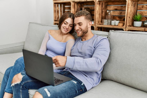 Young caucasian couple using laptop sitting on the sofa at home. - Photo, image