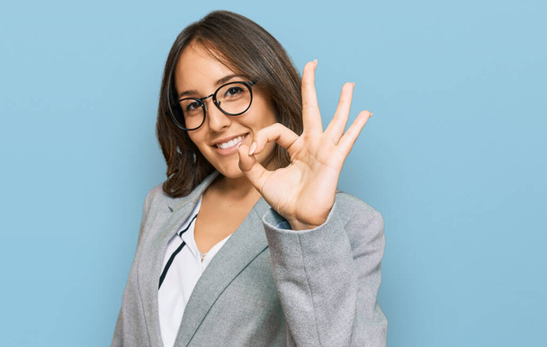 Jonge brunette vrouw draagt zakelijke kleding lachend positief doen ok teken met de hand en vingers. succesvolle uitdrukking.  - Foto, afbeelding