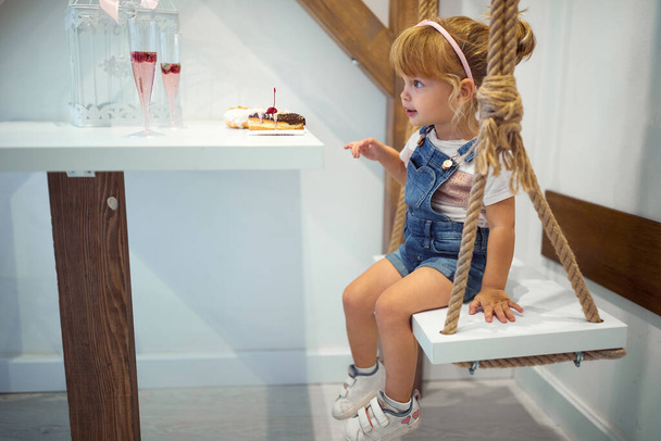 A little girl is sitting in a pastry shop and enjoying delicious donuts of irresistible appearance. Pastry shop, dessert, sweet - Foto, Imagem