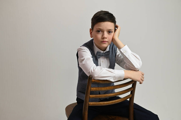 Portrait of a caucasian teenager boy on a white background sitting on a chair - Zdjęcie, obraz