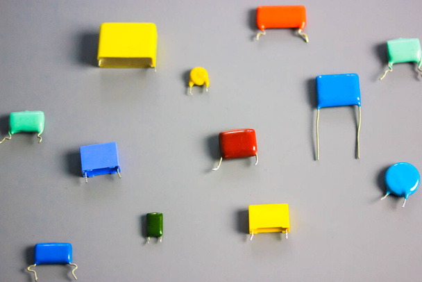 Subminiature polypropylene multicolored film capacitors on gray background flatly. Vintage electronic parts. Resistors and capacitors different size and color. HiFi Audio parts. Radio components.  - Photo, Image