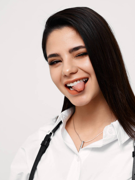 cheerful woman shows tongue on a light background and white shirt black suspenders - Photo, Image
