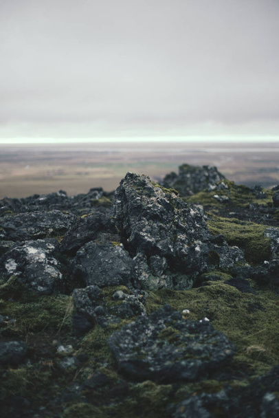 A vertical shot of a rocky terrain covered in mosses under a cloudy sky with a blurry background - Photo, Image