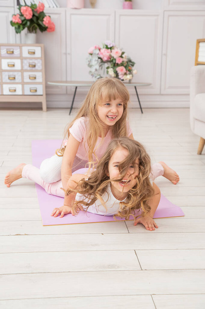 Vertical photo of couple little girls playing on yoga mat smiling in living room, healthy life habits and lifestyle concept. - Foto, Imagen