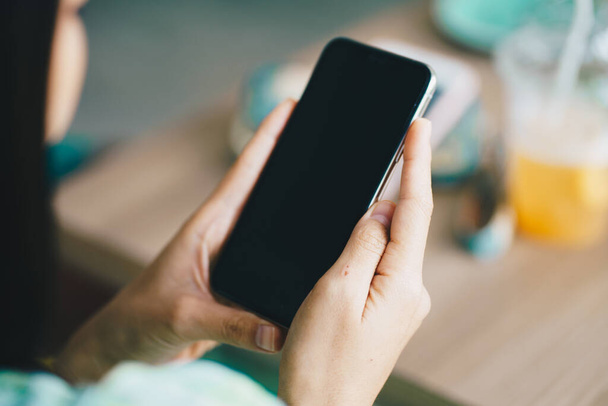 Woman hand holding smartphone black screen sittin in modern coffee shop blank screen phone close up - Photo, Image