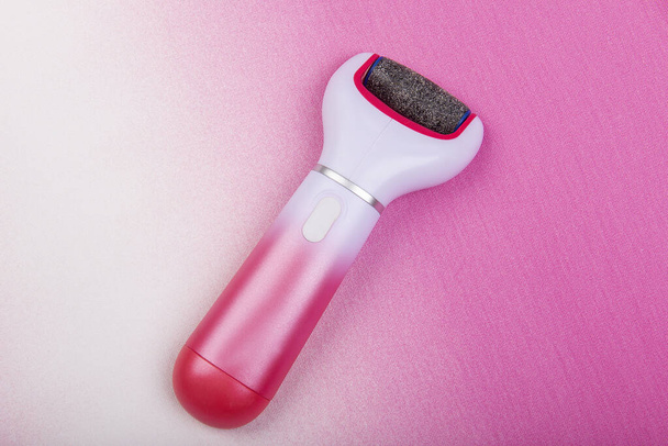 Care and cleansing of feet from rough, flaky skin. Electric sander with replaceable pedicure attachment at home, isolated pink background - Fotoğraf, Görsel