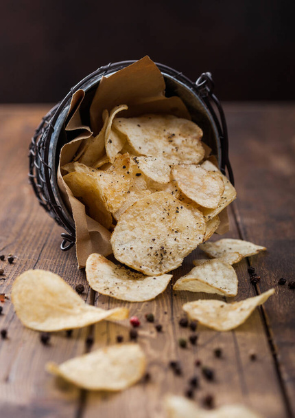 Crunchy potato crisps chips with black pepper taste in steel snack bucket on wooden table background. Macro - Φωτογραφία, εικόνα