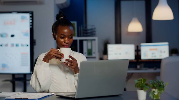 Чорна ділова жінка використовує навушники пити каву на відеоконференції
 - Фото, зображення