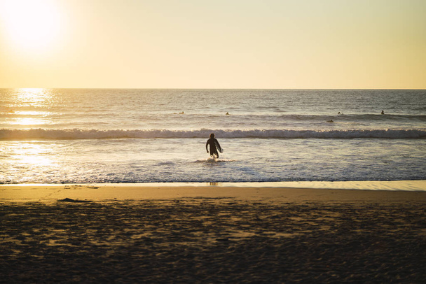 A surfer running into the water on a beach during a beautiful sunset - Fotoğraf, Görsel