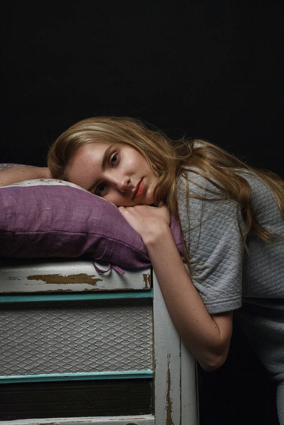 молода дівчина в сукні лежить на краю коробки на подушці, портрет моделі в приміщенні
 - Фото, зображення
