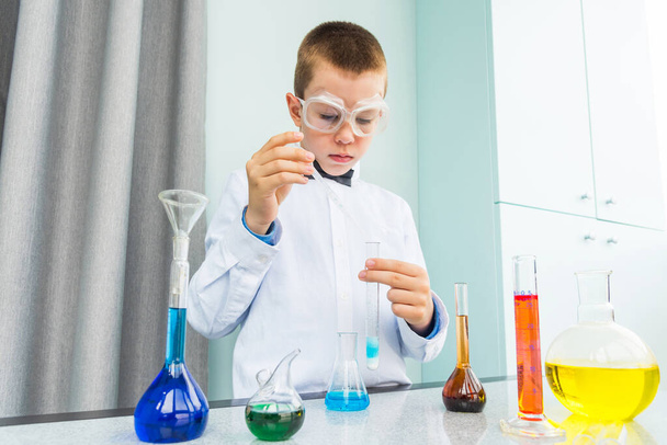 Dziecko prowadzi badania chemiczne w laboratorium domowym podczas nauki na odległość (kursy online). Mądry mały chłopiec naukowiec robi praktyczny eksperyment. - Zdjęcie, obraz