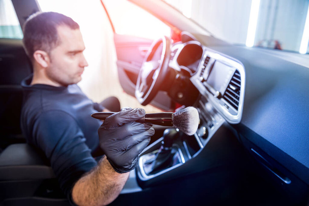 A car service worker cleans the car console with a special brush - 写真・画像