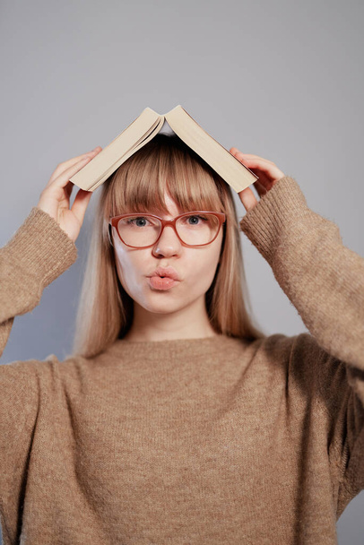 Αμφιβάλω συγκίνηση φοιτήτρια κορίτσι με βιβλίο στο κεφάλι και γυαλιά - Φωτογραφία, εικόνα