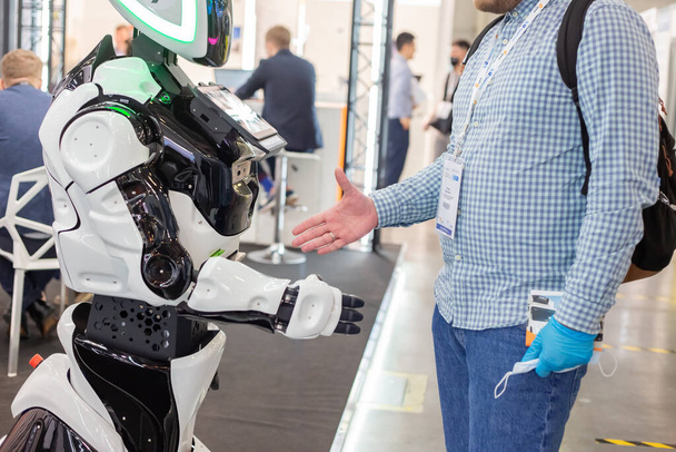 Moscow, Russia - 14 april 2021 : An exhibition visitor shakes hands with an intelligent robot at one of the stands at the International exhibition of transport and logistics services - Photo, image