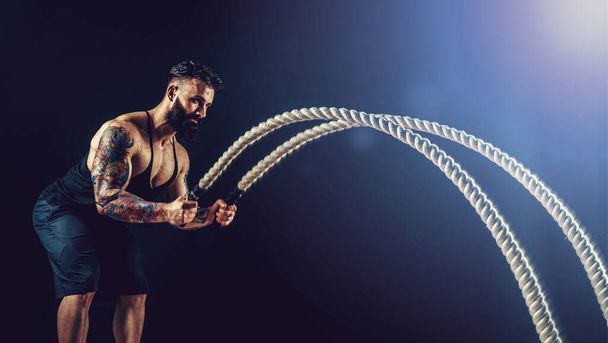 Muscular man working out with heavy rope. Photo of man with naked torso. Strength and motivation.  - Fotografie, Obrázek