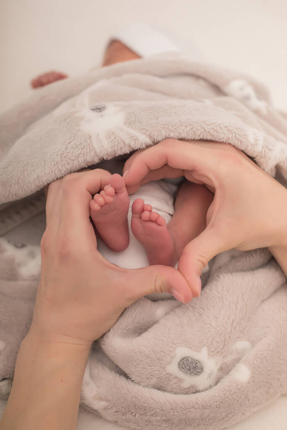 Las manos de una madre en forma de corazón alrededor de los pies de un bebé recién nacido. Primer plano de los pies del bebé en forma de corazón en las manos. - Foto, Imagen