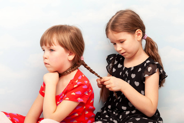 Dwójka małych dzieci w wieku szkolnym, siostry, rodzeństwo lub bliscy przyjaciele robiący sobie nawzajem włosy, plecący razem warkocze, zbliżenie. Rodzinna wspólnota, młode dzieci, koncepcja działalności integracyjnej rodzeństwa - Zdjęcie, obraz