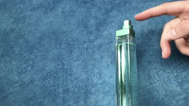 Vrouwelijke hand hagelslag parfum klikken op hen wijsvinger op een blauwe achtergrond. - Video