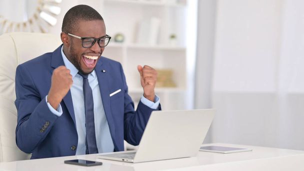 Ganar, Empresario africano celebrando el éxito en el ordenador portátil
  - Foto, Imagen