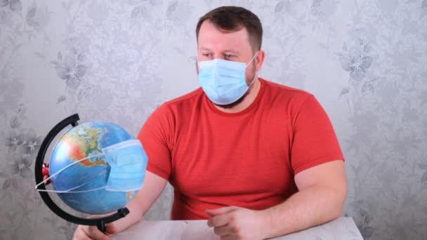 De mens is verdrietig over de ziektes op het plan en het gebrek aan reizen. man ziet er globe in beschermende masker en pandemische vaccin. Corona virus behandeling concept, injectie, klinische proeven tijdens een - Video