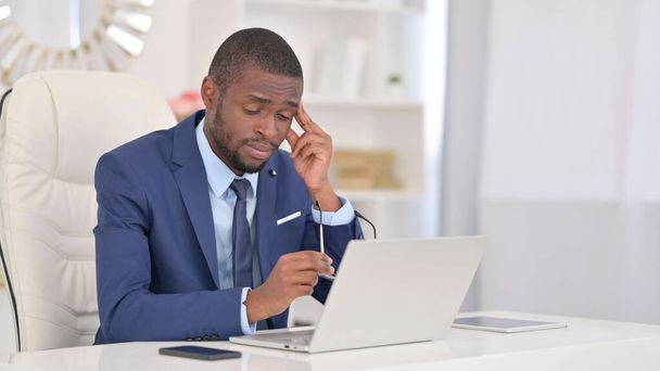 Молодий африканський бізнесмен з ноутбуком має головний біль у офісі  - Фото, зображення