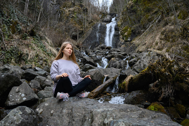 Dziewczyna siedzi na drzewie i medytuje w pobliżu górskiej rzeki w Abchazji - Zdjęcie, obraz