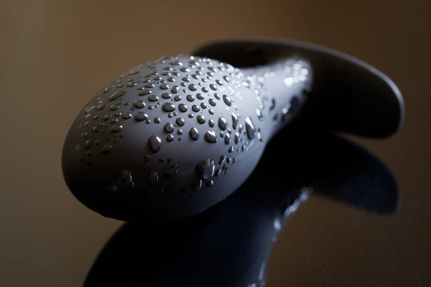 A black silicone butt plug with drops of moisture lies on a dark reflective surface. The concept of sex toys, lust and pleasure. Close-up - Photo, Image
