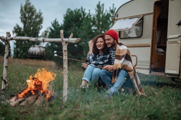 Paar in een geruite ruitjes roosteren marshmallows in brand in de buurt van de trailer huis. - Foto, afbeelding