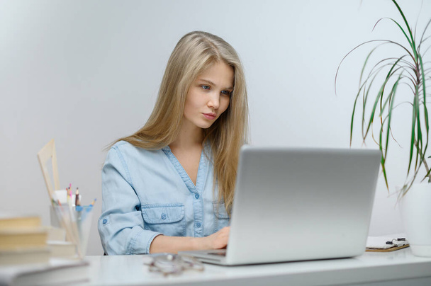 Une fille avec un ordinateur portable étudie dans une école en ligne. fond de la chambre blanche - Photo, image