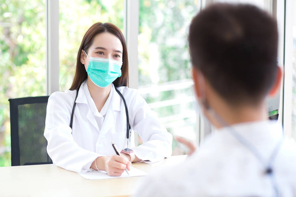 Asian beautiful woman doctor talking with a man patient about his pain and symptom while they put on a face mask to prevent Coronavirus disease in health care,pollution PM2.5,new normal and coronavirus protection concept. - Фото, изображение