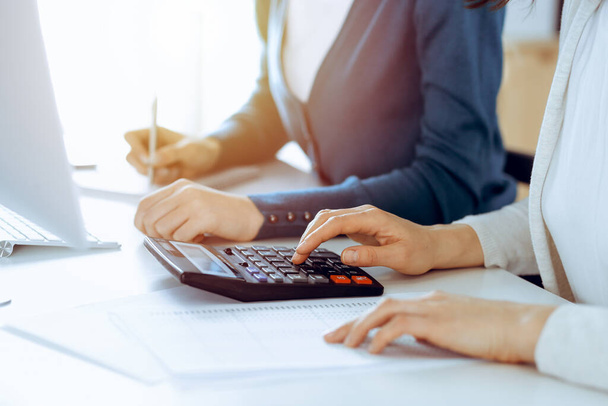 Accountant checking financial statement or counting by calculator income for tax form, hands closeup. Business woman sitting and working with colleague at the desk in office. Tax and Audit concept - Foto, imagen