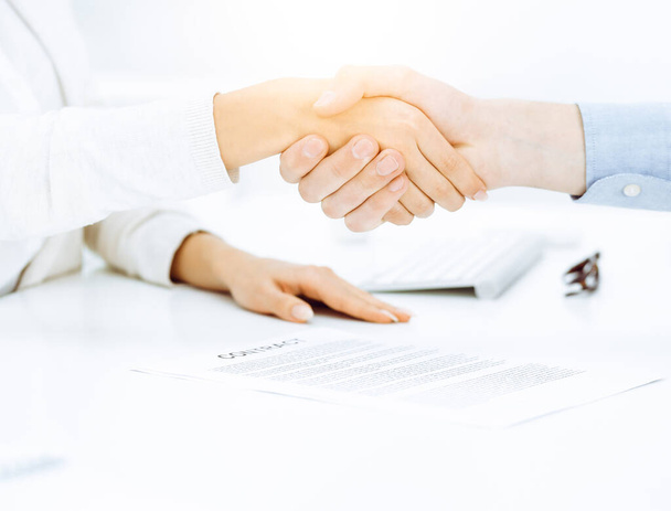 Casual dressed businessman and woman shaking hands after contract signing in sunny office. Handshake concept - Foto, imagen