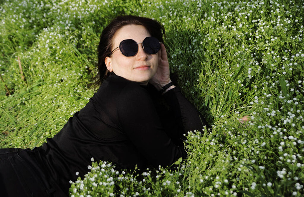 Güneş gözlüklü güzel genç bayan baharın tadını çıkarıyor. Dışarıda çimenlerde uzanan bir kadın. - Fotoğraf, Görsel
