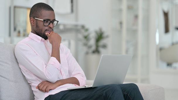 Pensive Afrikaanse man denken en werken op laptop thuis  - Foto, afbeelding