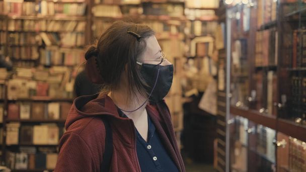 A nő szemüvegben és maszkban a vírus ellen úgy dönt, hogy könyvet vásárol antik boltban. - Fotó, kép