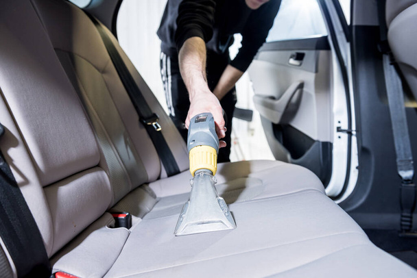 Worker cleans car interior with vacuum cleaner - Foto, imagen